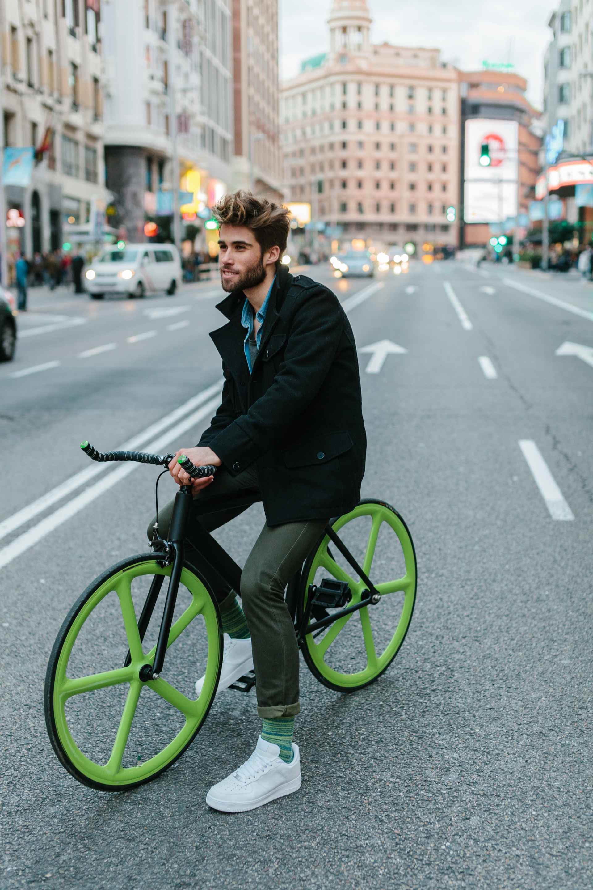 Man on a green bike ride through a city street.